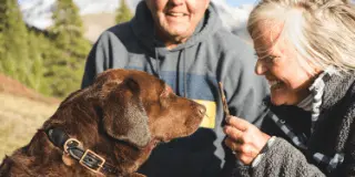 Picture of two people feeding a treat to a chocolate lab.